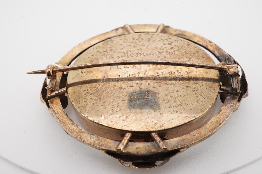 A Victorian yellow metal and black enamel oval mourning brooch, with plaited hair beneath a glazed panel, the back inscribed 'In Memory of Alex Rae died 21st Aug. 1848, A.B.', 53mm.